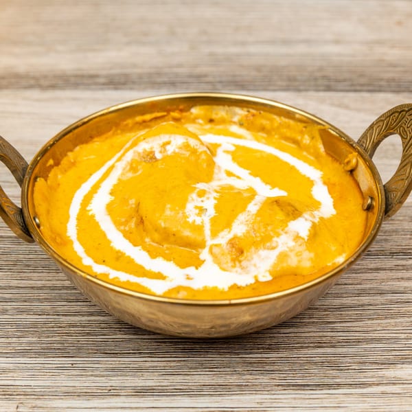 Magic Pepper's Indian butter chicken, garnished with cream swirls, in a brass serving bowl.