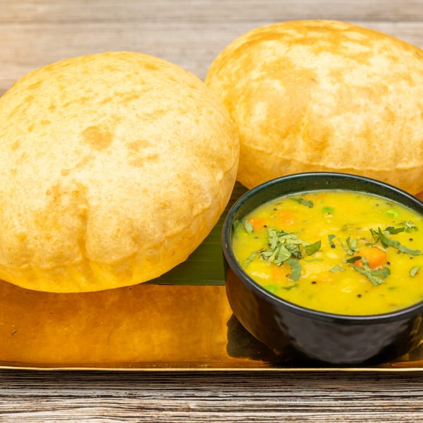 Two golden-brown Indian puri breads and a bowl of yellow vegetable curry on a gold tray.