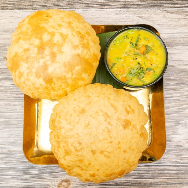 Two golden-brown Magic Pepper puri breads and a bowl of yellow vegetable curry on a gold tray.