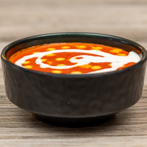 A black bowl of vibrant orange Indian curry with white cream swirls and yellow dots.