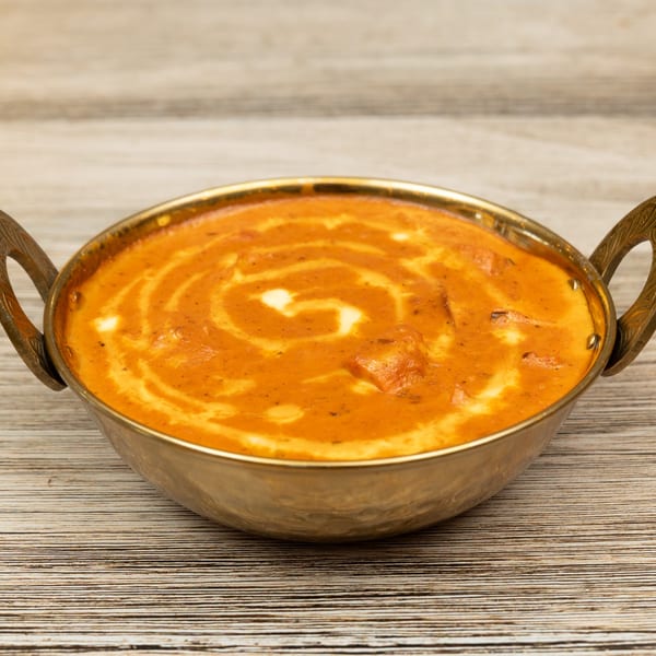 Magic Pepper's Indian butter chicken, a creamy orange curry with white swirls, in a brass bowl.