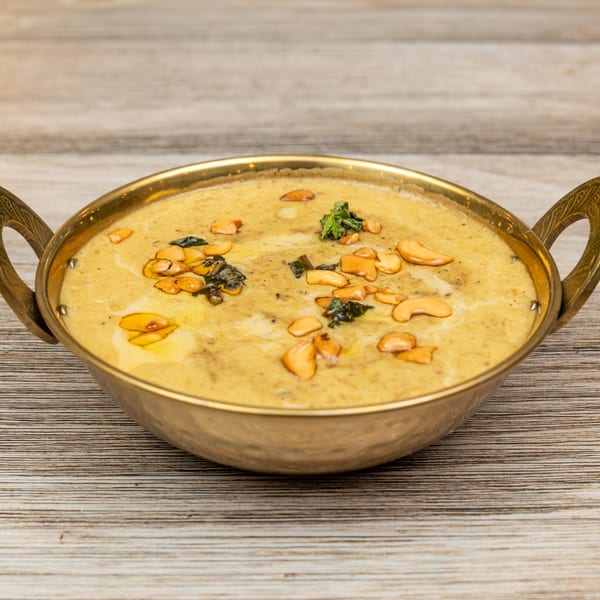 Magic Pepper's Indian curry, garnished with cashews and herbs, served in a brass bowl.