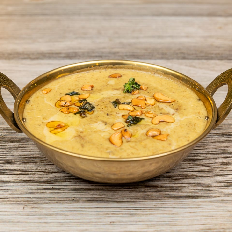 Magic Pepper's Indian curry, garnished with cashews and herbs, served in a brass bowl.